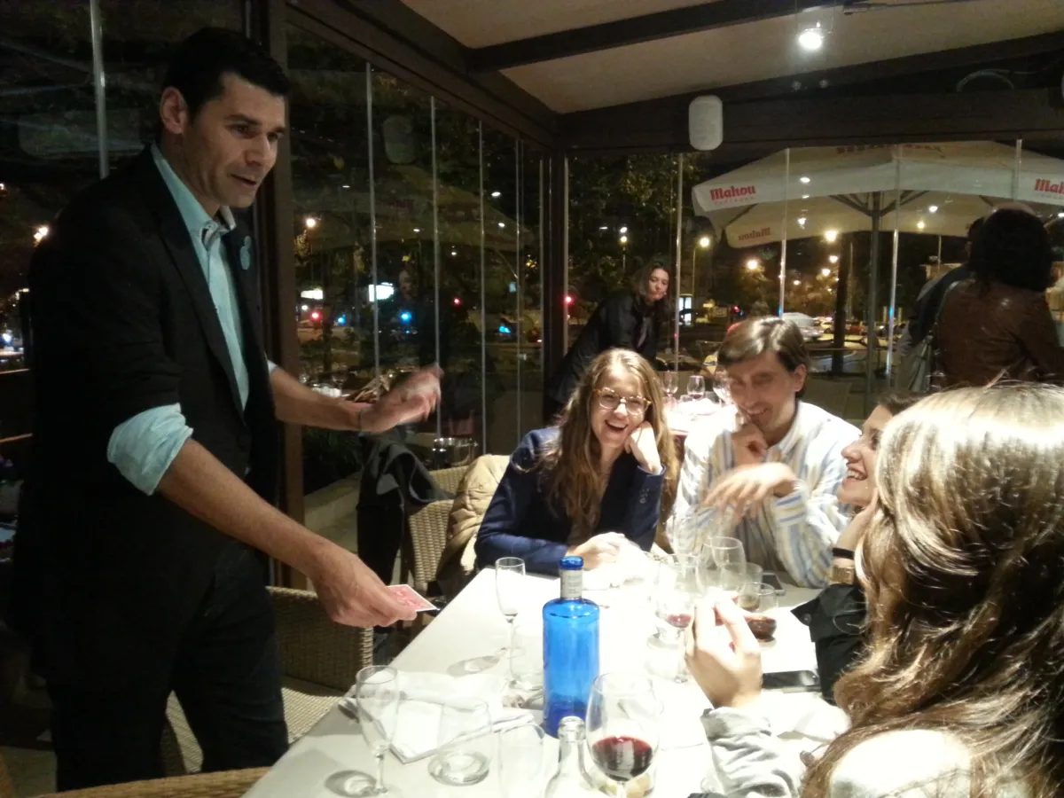 Mago haciendo magia de cerca en una mesa de compañeros que se ríen durante una cena de empresa