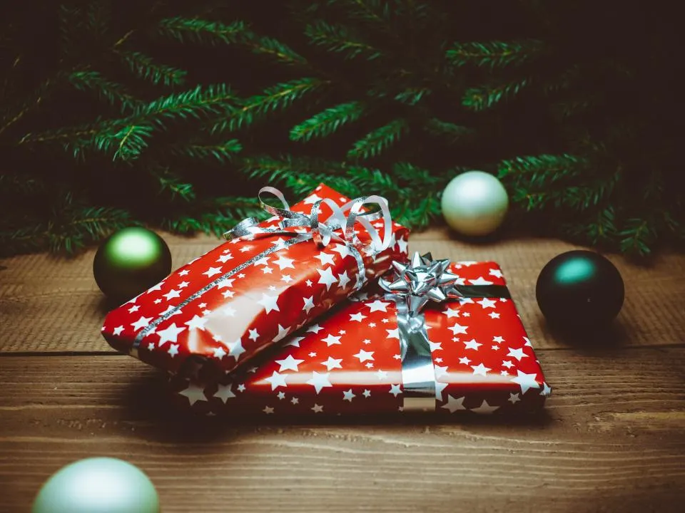 Dos regalos envueltos en papel rojo con estrellas junto a ramas de abeto y bolas de Navidad