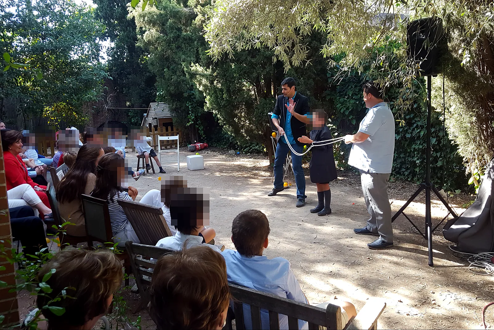 Mago haciendo magia con una cuerda junto a un niño voluntario ante los invitados de un cumpleaños en un jardín