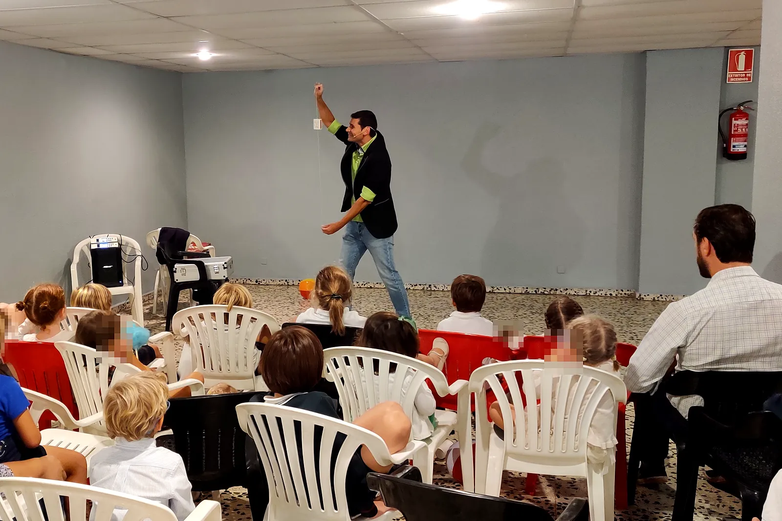 Mago actuando en una sala despejada ante niños sentados en sillas en una fiesta de cumpleaños
