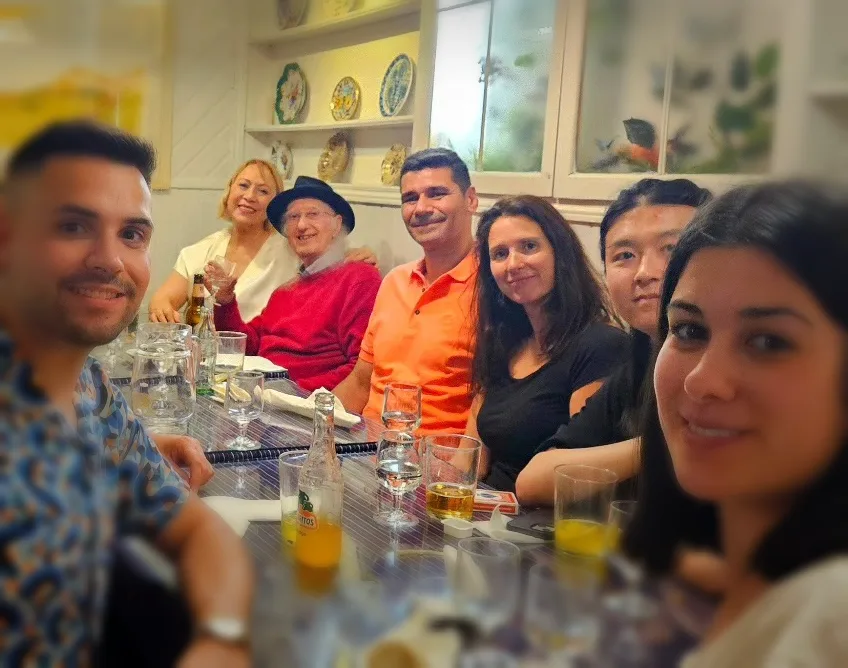 Juan Tamariz al fondo de una mesa larga con Julio Sánchez y un grupo de amigos en 2024