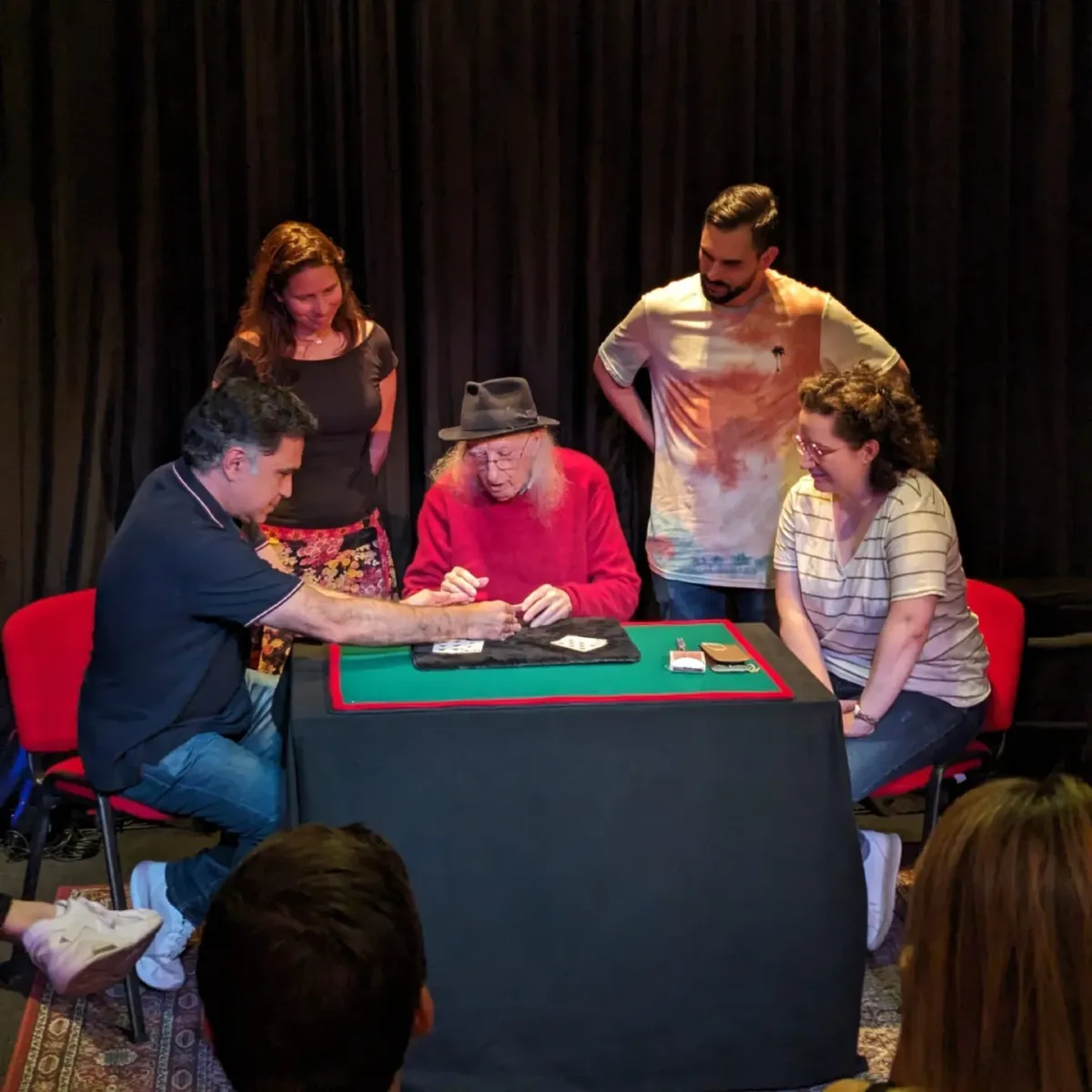 Juan Tamariz haciendo magia de cerca con cartas sobre un tapete, rodeado de público