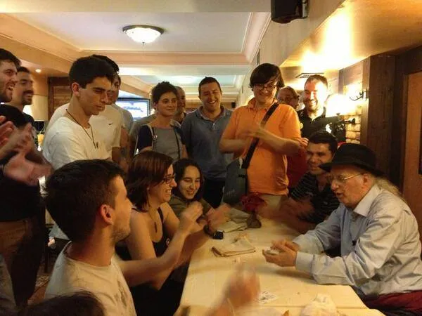 Juan Tamariz haciendo magia con cartas en una sobremesa rodeado de magos