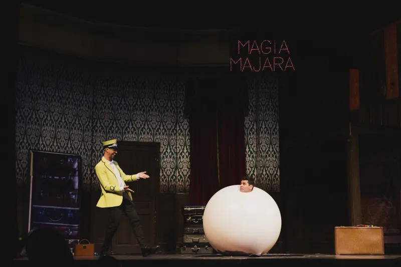 Un mago con uniforme de revisor junto a un globo blanco gigante en el escenario